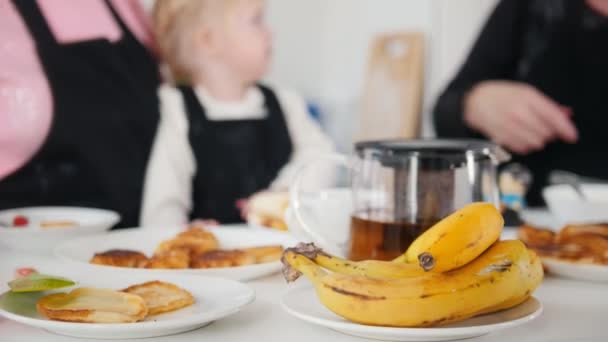 Família a comer panquecas e a beber chá. Frutas na mesa — Vídeo de Stock