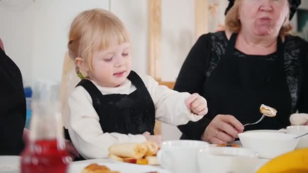 Familjen äter pannkakor. En liten flicka äter banan — Stockvideo