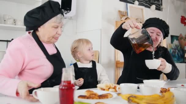 Familia comiendo panqueques y tomando té. Una niña comiendo plátano — Vídeos de Stock