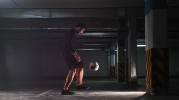 Υπόγειο πάρκινγκ. Αθλητικά ποδοσφαίρου άνθρωπος κατάρτισης δεξιοτήτων του ποδοσφαίρου. Αλίευση την μπάλα στην πλάτη του. Κλωτσάει την μπάλα από τον τοίχο — Αρχείο Βίντεο
