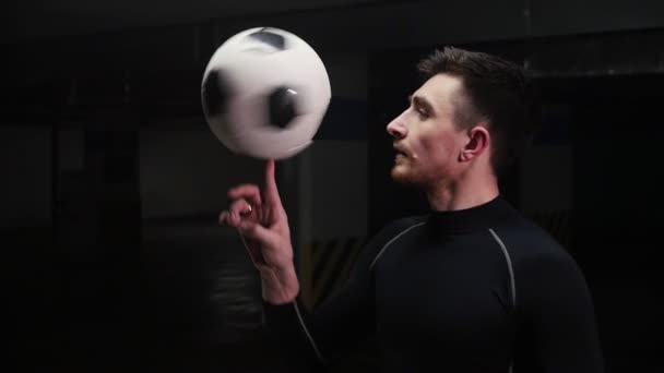 Mélygarázst. Egy fiatal foci férfi spinning a labdát az ujját, és keresi a kamera — Stock videók