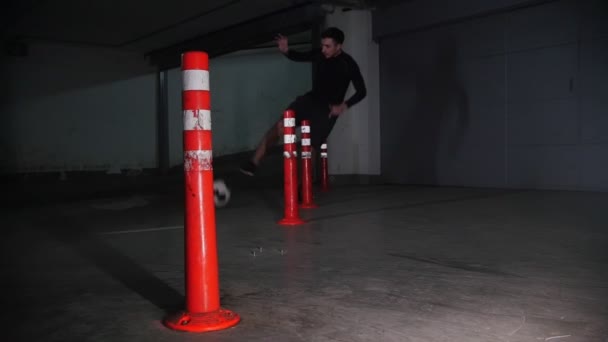 Parking souterrain. Un footballeur athlétique qui s'entraîne. Mener la balle contournant les obstacles — Video