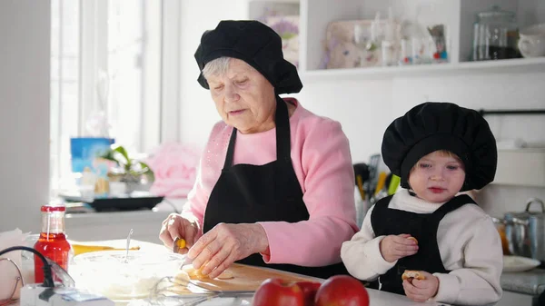 Familia en la cocina haciendo postres. Una anciana cortando el plátano — Foto de Stock