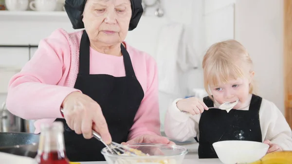 La familia hace panqueques. Una niña pequeña probando la masa — Foto de Stock