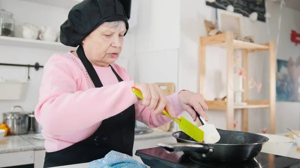 Una anciana haciendo panqueques en la cocina luminosa . — Foto de Stock