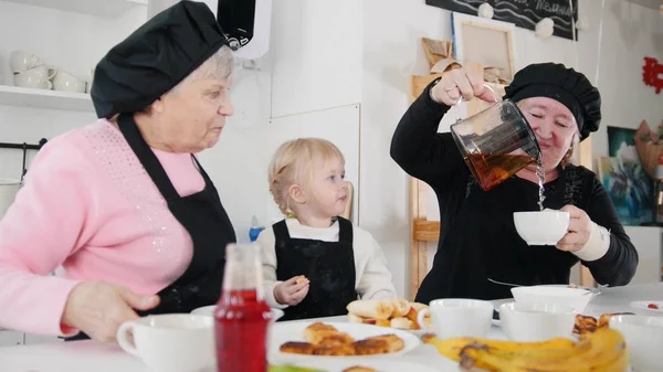 Familia comiendo panqueques y tomando té en la cocina. Verter el té en las tazas — Foto de Stock