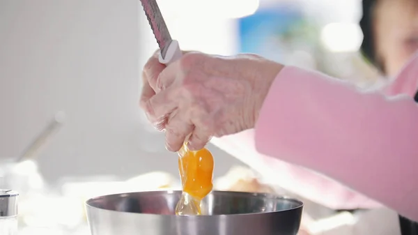 An old woman breaking an egg in the dough