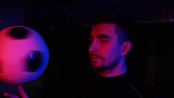 Ein junger Mann in der Tiefgarage dreht in Neonlicht den Ball am Finger. Blick in die Kamera — Stockvideo