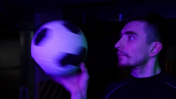 Ένας νεαρός άνθρωπος στο υπόγειο πάρκινγκ ρίχνει την μπάλα και την γυρίζει στο δάχτυλό του σε φωτισμό νέον — Αρχείο Βίντεο