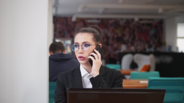 Concepto de negocio. Una mujer sentada junto a la mesa y hablando por teléfono — Vídeos de Stock