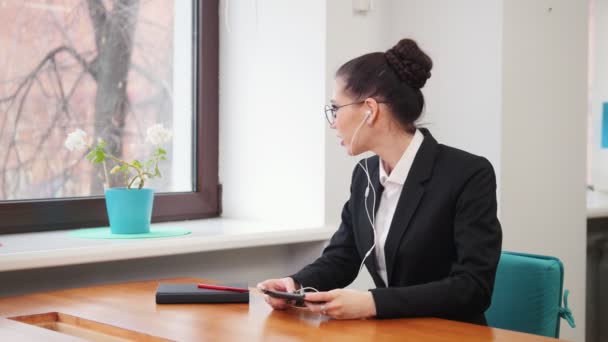 Geschäftskonzept. eine Frau mit Kopfhörern sitzt am Tisch und spielt ein Spiel auf ihrem Handy — Stockvideo