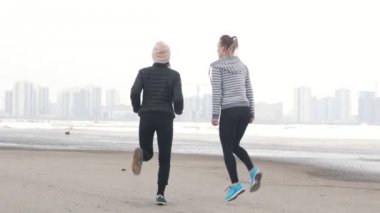İki atletik kadın sahilde ayakta ve koşu için ısınıyor. Soğuk hava