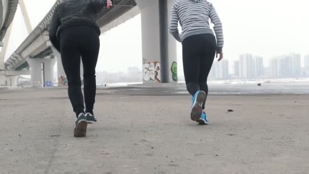 Duas mulheres atléticas a correr debaixo da ponte — Vídeo de Stock