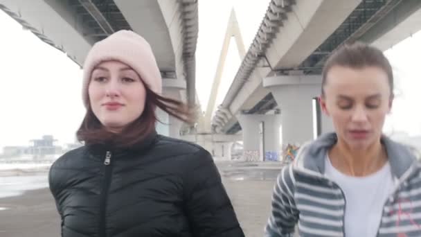 Δύο γυναίκες με μπουφάν που τρέχουν κάτω από τη γέφυρα — Αρχείο Βίντεο