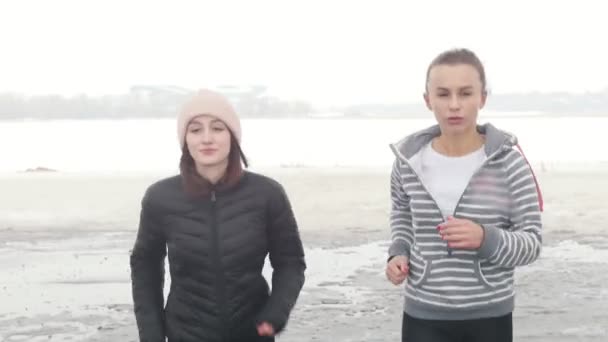 Twee atletische vrouwen in de herfst kleren lopen op een besneeuwd strand — Stockvideo