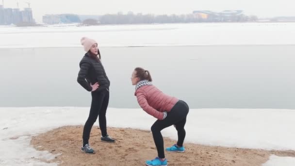 Twee slanke vrouwen staan op het besneeuwde strand en warming-up — Stockvideo