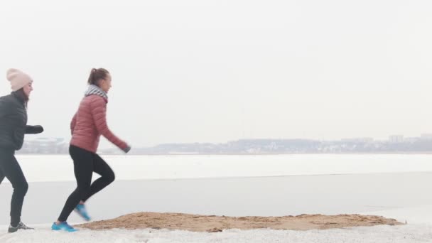 Dos mujeres atléticas corriendo en el lugar en una playa nevada — Vídeo de stock