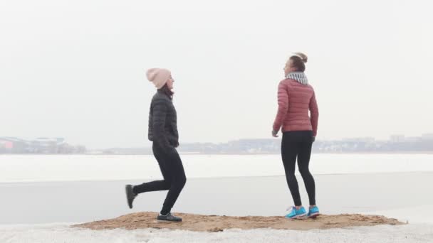 Twee atletische vrouwen die op een besneeuwd strand lopen. Staande op de grond en trekken hun handen omhoog — Stockvideo