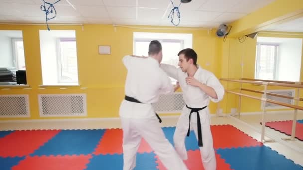 Two men training aikido skills. A man grabs his opponent and throws him on the floor — Stock Video