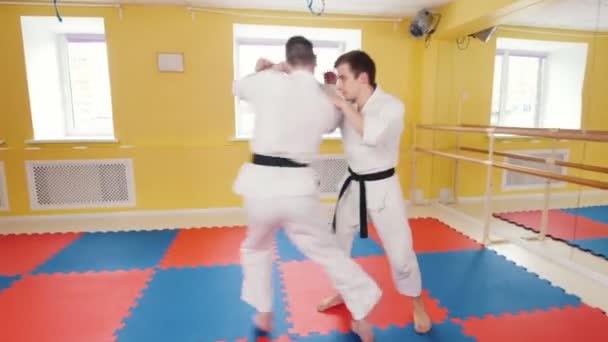 Två atletiska män tränar sin Aikido färdigheter i studion. En man tar tag i sin motståndare och kastar honom på golvet — Stockvideo