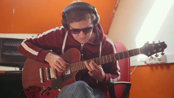 Um músico com auscultadores a trabalhar no estúdio. Tocar guitarra — Vídeo de Stock