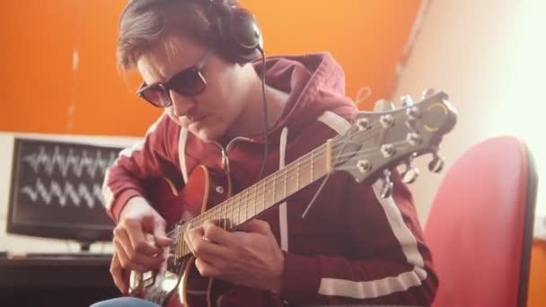 A musician man in headphones playing guitar and recording the sound in the studio — Stock Video