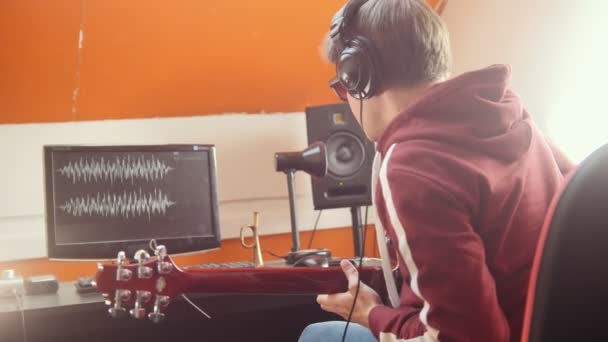 Muzyk w słuchawkach gra na gitarze i nagrywanie dźwięku w studiu. Patrząc na monitor — Wideo stockowe