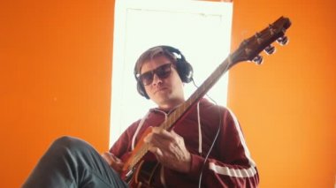 Kulaklıkta bir adam stüdyoda gitar çalarken gözlük giyiyor