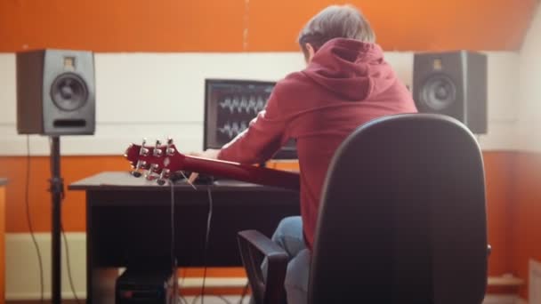 Un músico sentado junto a la computadora en el estudio y grabando una canción. Tomar auriculares y ponérselos en la cabeza — Vídeos de Stock