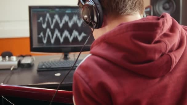 Muž ve sluchátkách, který sedí u počítače ve studiu zvukových nahrávek a nahrává píseň