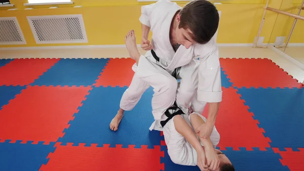 Twee atletische mannen trainen hun Aikido vaardigheden in de Studio. Een man liggend op de vloer en de bescherming tegen de hit — Stockfoto