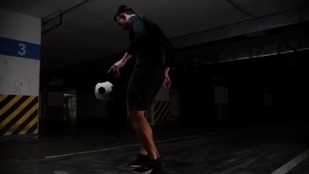 Ondergrondse parkeergarage. Een jonge voetbal man opleiding zijn voetbal vaardigheden. Het been gaat boven de bal — Stockvideo