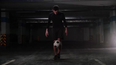 Topu tekmeleyen ve ayak üzerinde dengeleyen genç bir futbol adamı