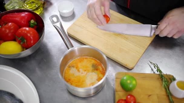 Ένας σεφ που δουλεύει στην κουζίνα. Κόβουμε τη ντομάτα στη μέση και προσθέτουμε τη σούπα — Αρχείο Βίντεο