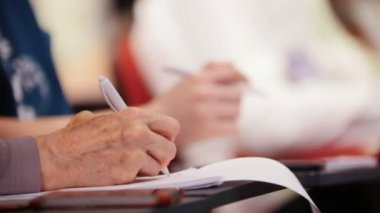 Salonda bir iş toplantısı var. Masanın yanında oturan ve defterde işaretler yapan yaşlı bir kadın.