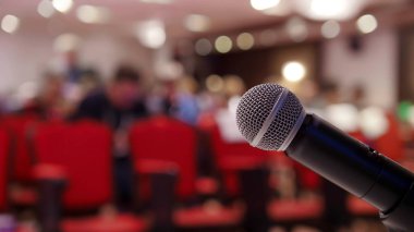 Salonda bir iş toplantısı var. Sandalyeler üzerinde oturan insanlar. Ön planda bir mikrofon