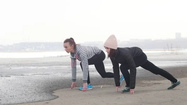 Δύο αθλητικές γυναίκες προετοιμάζονται για τρέξιμο σε μια χιονισμένη παραλία — Φωτογραφία Αρχείου