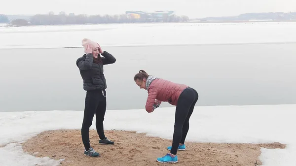 Duas mulheres magras em pé na praia nevada e aquecendo — Fotografia de Stock