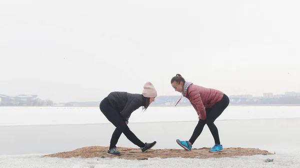 Duas mulheres magras de pé na praia nevada e se aquecendo para a corrida — Fotografia de Stock