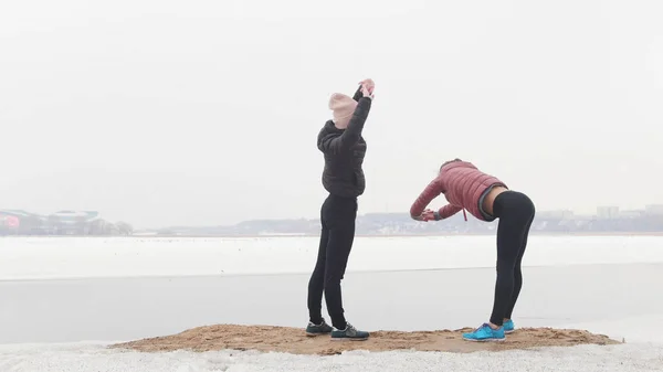 Δύο νεαρές αθλητικές γυναίκες στέκονται στην παραλία και θερμαίνουν. — Φωτογραφία Αρχείου