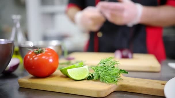 Un chef trabajando en la cocina. Cortar la cebolla. Un tomate y lima en primer plano — Vídeos de Stock