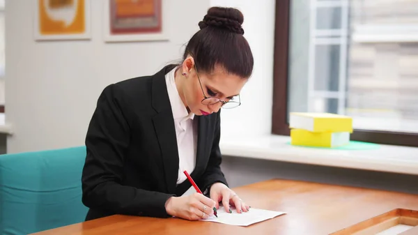 Бизнес-концепция. Женщина в очках сидит за столом и заполняет документы — стоковое фото