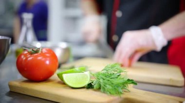 Mutfakta bir aşçı domates kesiyor. Ön planda domates ve kireç
