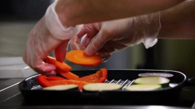 Mutfakta çalışan bir şef. Bir kişi tava üzerinde sebze koyar