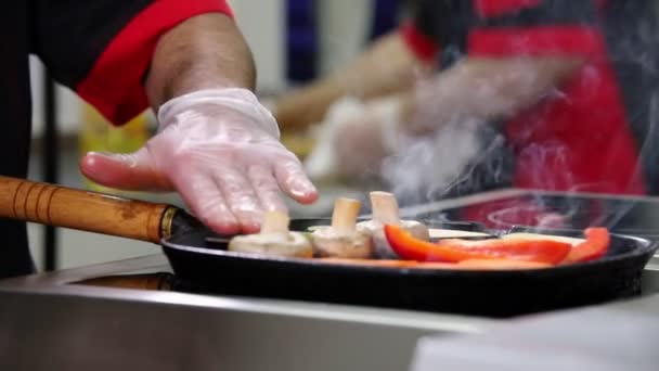 Повар, работающий на кухне. Человек нагревает грибы и овощи — стоковое видео