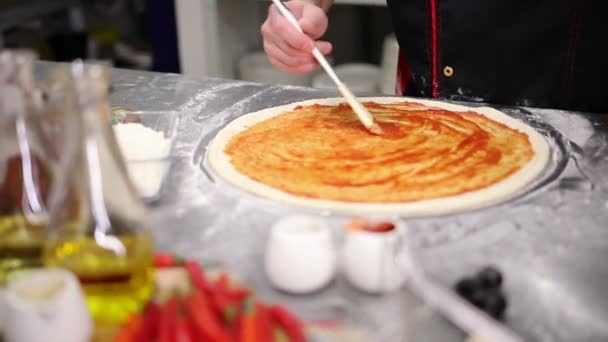 Restaurant keuken. Een chef-kok zet de tomatensaus op het deeg — Stockvideo