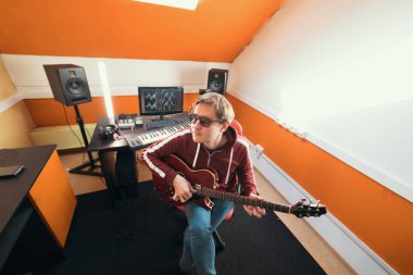 Gözlük bir adam kayıt stüdyosunda gitar oynuyor