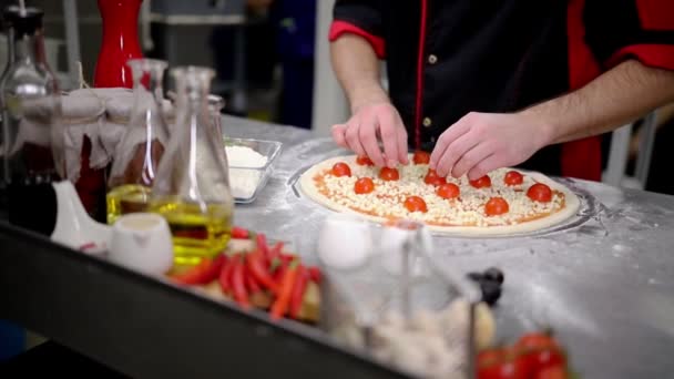 Étterem konyha. A szakács a sajtot és a paradicsomot a pizza tetejére — Stock videók