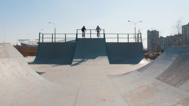 Dva muži na kole začínají jezdit z kopce na skateparku. — Stock video