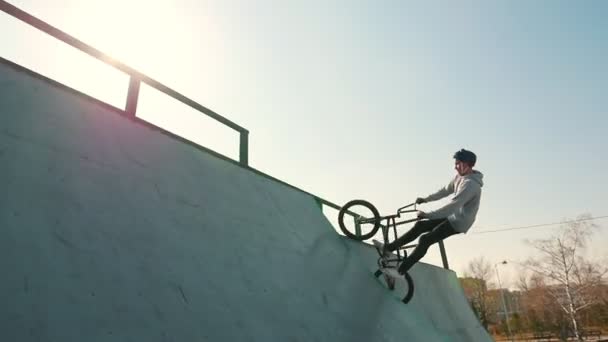 Ein BMX-Fahrer trainiert sein Können im Skatepark. rast auf und ab, macht einen Salto und geht vor hellem Sonnenhintergrund unter — Stockvideo